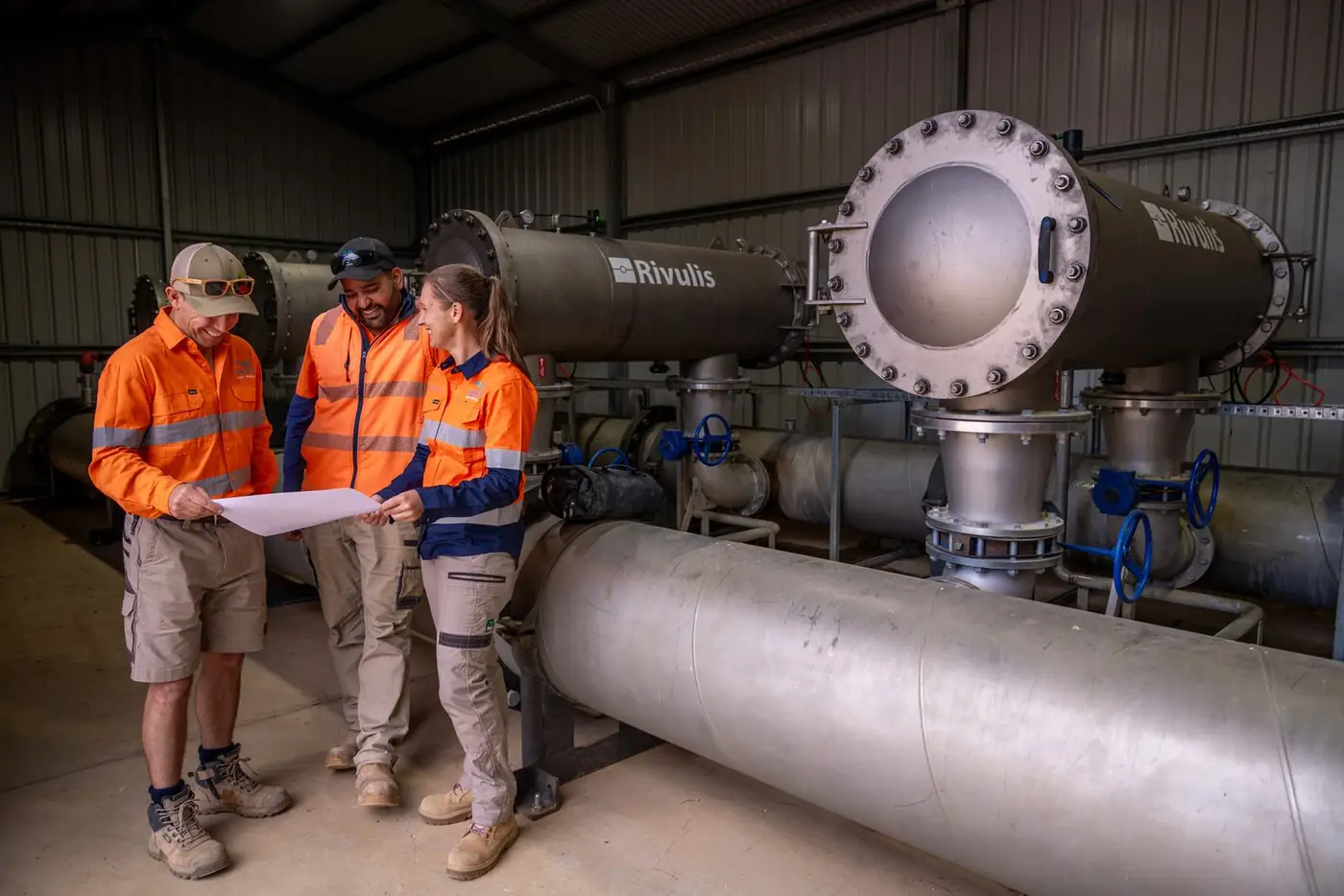 Three Ardal staff reviewing a plan beside large filters in a pump shed