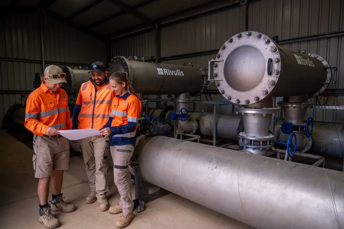 Three Ardal staff reviewing a plan beside large filters in a pump shed